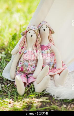 Zwei Spielsachen Kaninchen, ein Junge und ein Mädchen, die im Stil von Tilda gefertigt wurden, sitzen in der Natur am Fuß des Zeltes. Stockfoto