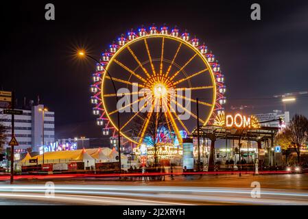 Hamburg, Deutschland-11232021:Nachtaufnahme des Eingangs zum hamburger Volksfest DOM mit dem Riesenrad und den Lichtspuren der vorbeifahrenden Ca Stockfoto