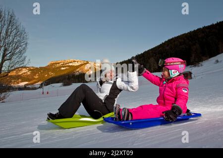 LANs-en-Vercors (Südostfrankreich): Frau und 6-jähriges Mädchen, Mutter und Tochter, die abends auf einer Skipiste des Vercors-Massivs Schlittenfahren. Stockfoto