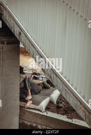 Bangkok, Thailand - Apr 02, 2022 : erschöpfter müder Bauarbeiter schläft während der Arbeitspause unter der Brücke auf der Matte bei einer Projektarbeit ein Stockfoto