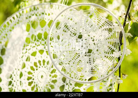 Handgefertigte gehäkelte Traumfänger, die an einem sonnigen Frühlingstag an einem blühenden Baum in einem Obstgarten hängen. Stockfoto