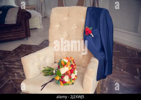 Der Brautstrauß und die Jacke des Bräutigams mit einem Boutonniere auf einem antiken gepolsterten Sessel im Schlafzimmer. Stockfoto