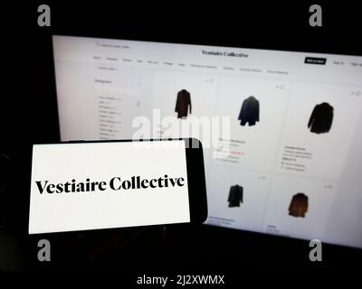Person, die Mobiltelefon mit Logo des französischen E-Commerce-Unternehmens Vestiaire Collective SA auf dem Bildschirm vor der Webseite hält. Konzentrieren Sie sich auf die Telefonanzeige. Stockfoto