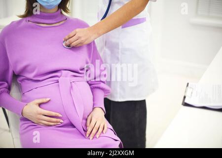 Arzt hört auf den Herzschlag einer Schwangeren Frau mit Stethoskop während eines Vorsorgetermins im Krankenhaus, zugeschnittenes Bild. Herzkrankheit in der Schwangerschaft Stockfoto