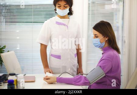 Arzt, der den Blutdruck einer Schwangeren misst, während er sie zu Hause besucht, Therapeut, der die werdende Mutter während des Vorsorgetermins untersucht Stockfoto