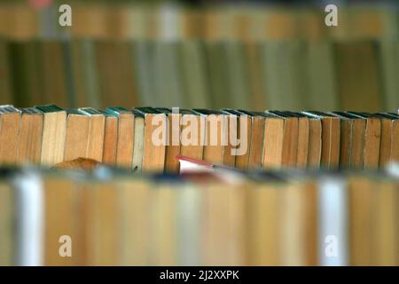 Verblasste Literatur. Reihen alter und gelbfärbiger Taschenbücher, die auf einem Buchmarkt ausgestellt sind. Abstrakte Schärfentiefe mit Kopierbereich. Stockfoto