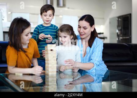 Konzentrierte Eltern und Kinder spielen Brettspiele, während sie Freizeit zu Hause genießen. Glückliche junge kaukasische Familie mit kleinen Kindern, die in der Sonne sitzen Stockfoto