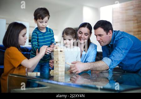 Konzentrierte Eltern und Kinder spielen Brettspiele, während sie Freizeit zu Hause genießen. Glückliche junge kaukasische Familie mit kleinen Kindern, die in der Sonne sitzen Stockfoto