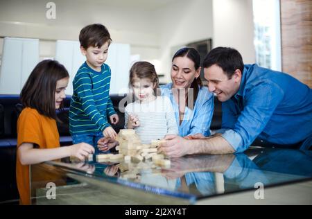 Konzentrierte Eltern und Kinder spielen Brettspiele, während sie Freizeit zu Hause genießen. Glückliche junge kaukasische Familie mit kleinen Kindern, die in der Sonne sitzen Stockfoto