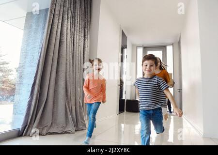 Glückliche Familie, die in der Halle läuft. Lustige Kinder springen mit Karton-Box, Eltern lachen, spielen mit Kindern Spaß haben zusammen bewegen sich im neuen Haus. Hypothek Stockfoto