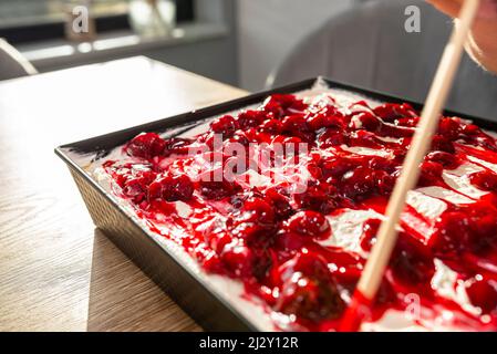 Eine Frau verwendet einen Stock, um einen fertigen japanischen Kuchen mit Quark, Schlagsahne und Obstkirschsoße zu dekorieren. Stockfoto