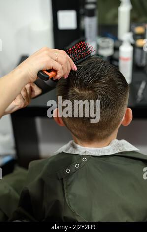 Teenager bekommt einen Haarschnitt während einer Pandemie in einem Friseurladen, einen Haarschnitt und trocknet Haare nach einem Haarschnitt, styling Haare nach einem Haarschnitt mit einem Haartrockner. Stockfoto