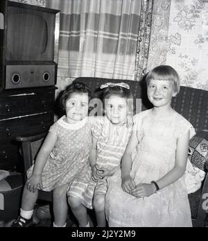 1962, historisch, in einem vorderen Raum, drei junge Mädchen sitzen zusammen auf einem Sofa, ein Fernseher der Ära sitzt in der Ecke, Stockport, Manchester, England, Großbritannien Stockfoto