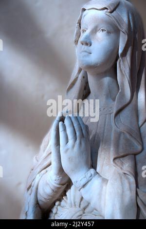 Mondbeleuchtete Madonna. Mondschein, der auf das Gesicht und die Hände einer Statue der Madonna beim Gebet fällt. Stockfoto