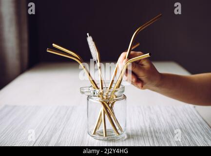 Kind Hand Nehmen Sie goldenen Metall Trinkhalm aus Glas in der Küche zu Hause. Nachhaltiges Lifestyle-Konzept. Stockfoto