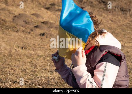 Das kleine Mädchen bedeckte ihr Gesicht mit der blau-gelben ukrainischen Flagge, Freedom Concept. Stockfoto