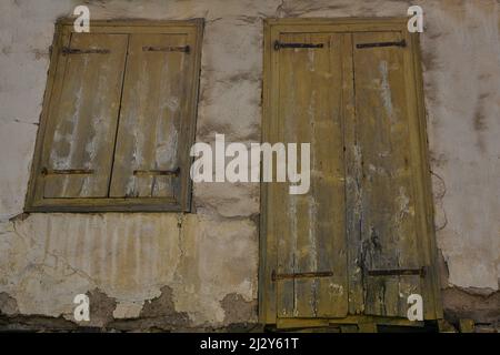 Alte ockerfarbene Holztüren und Fensterläden an einer alten Stuckwand in Andritsaina, Peloponnes, Griechenland. Stockfoto