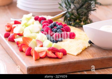 Eine Platte mit geschnittenen Früchten und verschiedenen Beeren, die auf einem Holzbrett angeordnet sind. Eine gesunde Frühstücksauswahl für Gäste in einem Hotel. Stockfoto