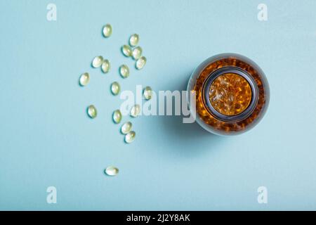 Ölkapseln mit Vitamin d oder Omega 3 in einer Glasflasche auf blauem Hintergrund. Blick von oben. Stockfoto