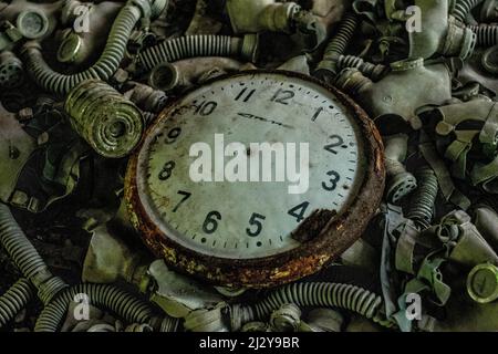 Nahaufnahme einer rostigen alten Uhr, umgeben von Gasmasken in Tschernobyl Stockfoto