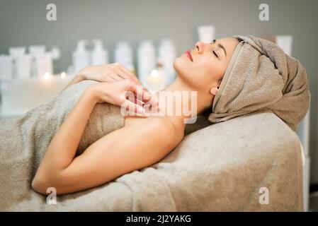 Seitenansicht einer entspannten Frau mit einem Handtuch auf dem Kopf, das mit geschlossenen Augen unter dem Plaid liegt, während Sie sich im Spa-Salon ausruhen Stockfoto