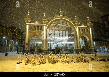 Verschneite Nacht, ein Marktgebäude mit einem Fahrradständer mit vielen komplett schneebedeckten Fahrrädern Stockfoto