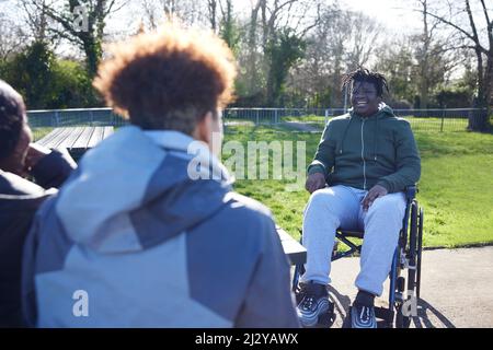 Teenage Boy In Wheelchair Aufhängen Reden Und Lachen Mit Freunden Im Park Stockfoto