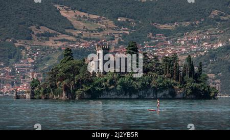 Frau paddelt auf SUP-Bord vor dem Castello della Isola di Loreto Schloss auf der Insel im Iseosee in Italien Stockfoto