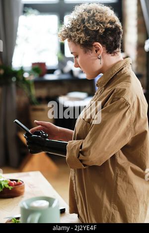 Mädchen mit Prothesenarm, das ihr Mobiltelefon benutzt, um Fotos von Essen auf dem Tisch in der Küche zu machen Stockfoto