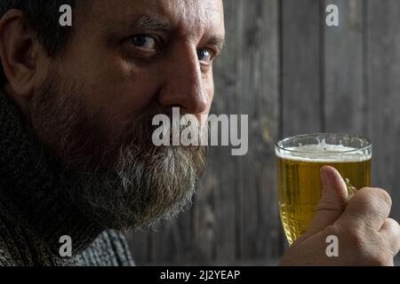 Bärtiger, brutaler Erwachsener, der aus dem Becher leichtes Bier trinkt Stockfoto