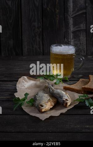 Gesalzener, getrockneter Vobla-Fisch mit bernsteinfarbenem Bier auf dunklem Holzboden mit Brot auf dem Tisch Stockfoto