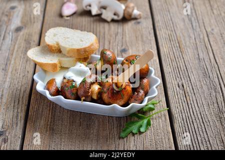 Gebratene Pilze mit Schalotten und Petersilie, serviert mit einer Knoblauch-Dip-Sauce in einem wiederverwendbaren Tablett Stockfoto