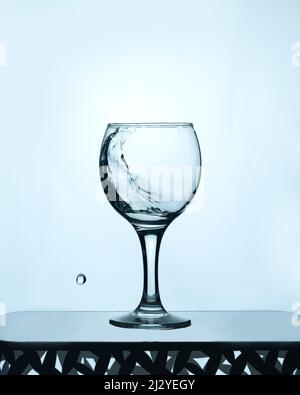 Ein Glas sauberes Wasser mit einem Spritzer auf einem hellen Hintergrund Stockfoto