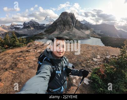 Hübscher asiatischer männlicher Reisender, der auf dem Hügel mit dem Berg assiniboine im Nationalpark von BC, Kanada, ein Selfie-Porträt macht Stockfoto