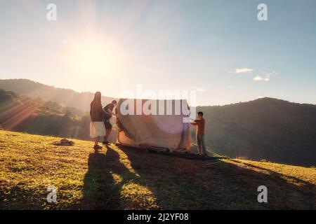 Eine Gruppe von Freunden, die ein Zelt auf dem Campingplatz Hügel im Sonnenuntergang auf dem Land aufschlagen Stockfoto