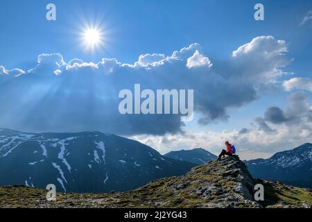 Wanderfrau auf Felsen sitzend, Wolkenstimmung im Hintergrund, Königstuhl, Nockberge, Nockberge-Trail, UNESCO Biosphärenpark Nockberge, Gurktaler Alpen, Kärnten, Österreich Stockfoto