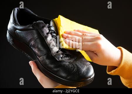 Ein Mann wischt schwarze Lederschuhe mit einem gelben Schuhlappen ab. Reinigung von Staub, Schuhpflege Stockfoto