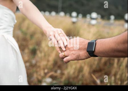 Nahaufnahme Braut und Bräutigam stehen vor der Hochzeit mit Händen im Wald draußen. Hochzeitskleid, fröhliche Paar Stockfoto