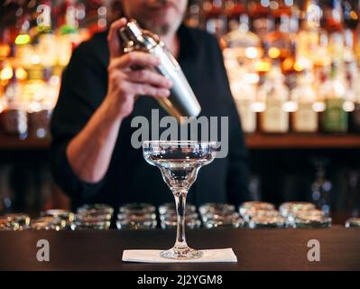 Der Barkeeper macht einen Cocktail mit einem Shaker hinter der Theke im Pub Stockfoto