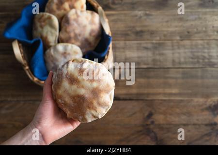 Die Hände der Frau legen hausgemachtes Pita-Brot in einen Holzkorb auf einen alten Holztisch. Speicherplatz kopieren. Stockfoto