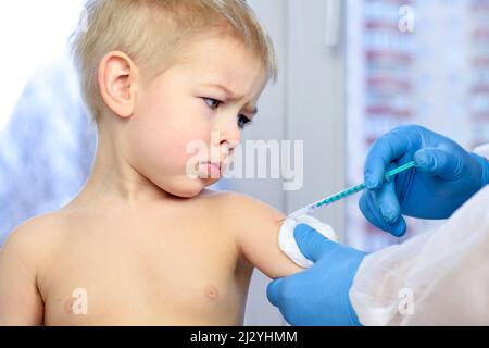 Arzt, der die Impfung in den Arm eines kleinen Jungen einspritzt. Coronavirus-Impfung. Arzt, der Kind impft. Kleiner Junge, der eine Grippeimpfung erhalten hat. Stockfoto