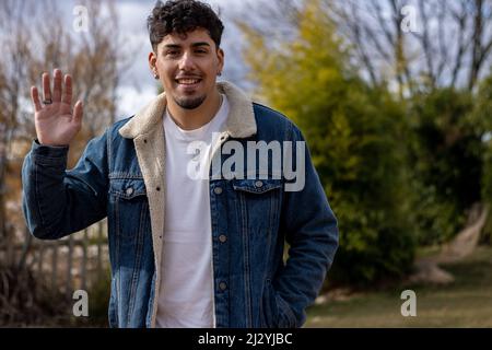Ein hispanischer junger Mann winkt und lächelt vor der Kamera Stockfoto