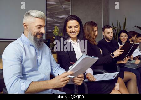 Lächelnde Menschen kommunizieren während der Pausen während einer Geschäftsschulung oder eines Seminars miteinander. Stockfoto