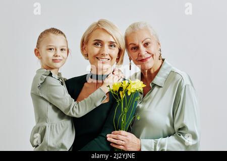 Minimalporträt von drei Frauen in der Familie, die Blumen in der Hand halten und die Kamera im Studio anlächeln Stockfoto