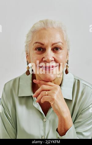 Vertikales Porträt einer eleganten älteren Frau, die die Kamera anschaut und lächelt, während sie im Studio posiert Stockfoto