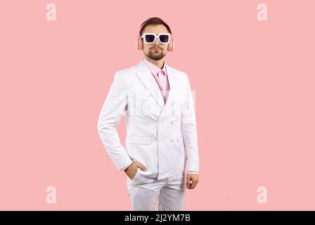 Hübscher junger Mann mit weißem Anzug, Sonnenbrille und Kopfhörern, der Musik hört Stockfoto