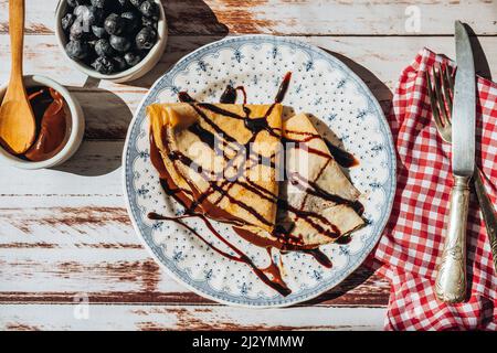 Teller zwei exquisite hausgemachte Pfannkuchen oder Crepes mit Mandelcreme und Schokolade mit Schokoladenfäden bedeckt gefüllt. Stockfoto