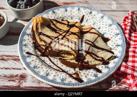 Teller zwei exquisite hausgemachte Pfannkuchen oder Crepes mit Mandelcreme und Schokolade mit Schokoladenfäden bedeckt gefüllt. Stockfoto
