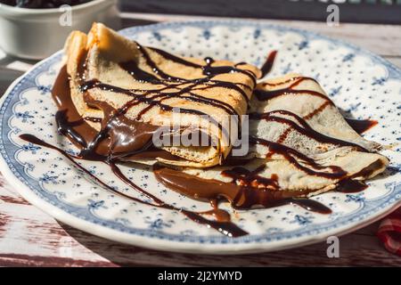Teller zwei exquisite hausgemachte Pfannkuchen oder Crepes mit Mandelcreme und Schokolade mit Schokoladenfäden bedeckt gefüllt. Stockfoto