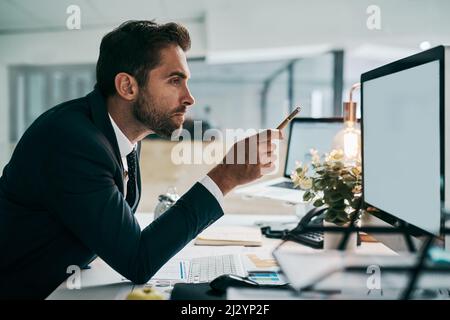 Er hat seine Augen auf die Arbeit gerichtet. Aufnahme eines fokussierten jungen Geschäftsmannes, der mit einem Stift auf einen Computerbildschirm zeigt, während er im Büro sitzt Stockfoto